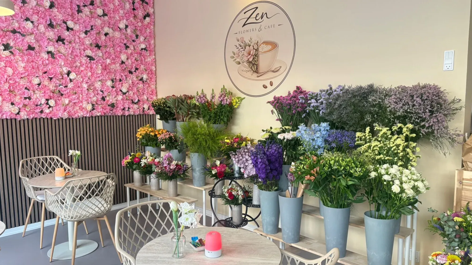 Butikken med lyserød blomstervæg, caféborde og spande med blomster
